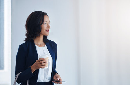Making moves that will have her soar in her career. a young businesswoman using a cellphone in an office.の写真素材