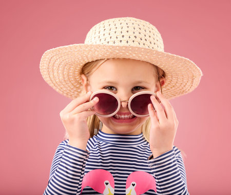 Vacation, portrait of child in studio with sunglasses and fun clothes and hat isolated on pink...