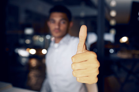 Business man, night and thumbs up in office success, thank you or tech support for solution, like or goals. Professional person in workplace bokeh, career portrait vote, ok or agreement hand or emojiの写真素材