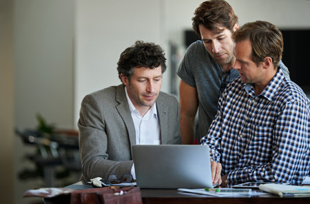 Adding some final touches to their project. three male coworkers working on a laptop together.の写真素材