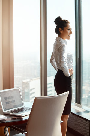 Success is its own reward. an attractive young businesswoman standing with her hands on her hips in the office.の写真素材