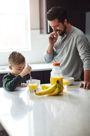 Eat up. a young boy and his father having breakfast in the kitchen.の写真素材