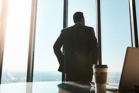 Success comes from maintaining a strong focus on your dreams. Rearview shot of a young businessman looking out the window in an office.の写真素材
