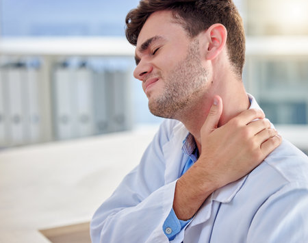 Tired, stress and man or doctor neck pain in office overworked, burnout or tension for healthcare problem. Medical professional worker, frustrated person or nurse with muscle injury at deskの写真素材