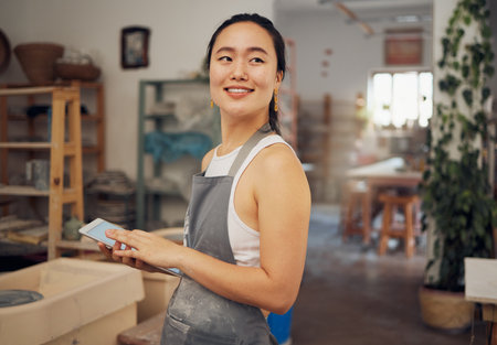 Tablet, small business and woman in pottery workshop for ceramic startup, research and online website. Creative art, ecommerce and asian lady with tech to sell clay, sculpture and handmade productsの写真素材