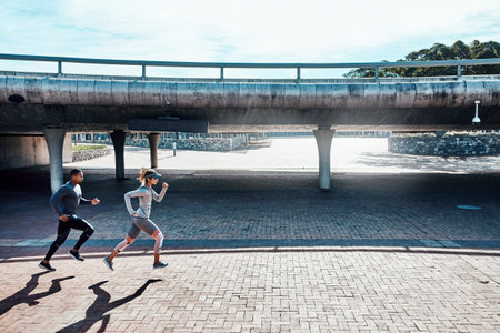 Owning their workout. Full length shot of two young and athletic young people running through the city.の写真素材