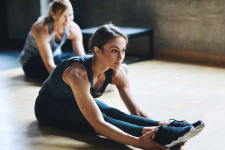 Stay loose. Stay active. Full length shot of two attractive young women stretching before their workout in the gym.の写真素材