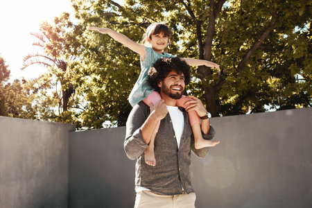 Dad makes every day so exciting. a father giving his little daughter a piggyback ride outdoors.の写真素材
