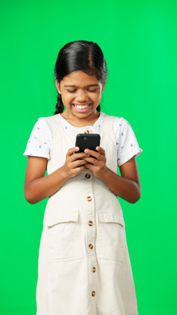 Happy, green screen and girl with smartphone, typing and laughing against a studio background. Mobile app, young person and female child with cellphone, connection and communication on social mediaの写真素材