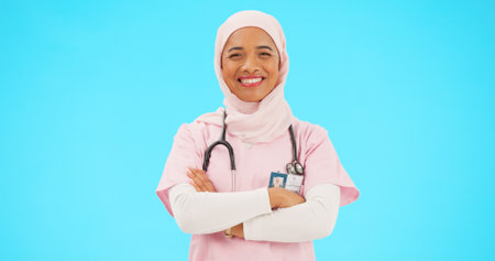 Muslim woman, face and nurse smile with arms crossed in studio isolated on blue background mockup. Portrait, medical professional and confident, happy and proud Islamic person or surgeon from Turkey.の写真素材