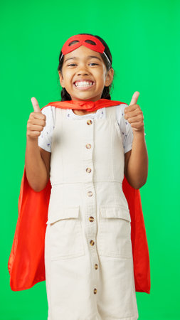 Little girl, superhero and thumbs up on green screen for success against a studio background. Portrait of happy adorable child or kid in hero cosplay showing thumb emoji, yes sign or like on mockupの写真素材