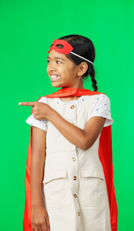 Face, superhero costume and girl pointing on green screen in studio isolated on a background. Smile, cosplay character and happy child or kid in cape point to mockup, product placement or marketing.の写真素材