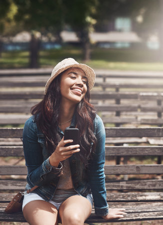 Gotta soak up these carefree days. an attractive young woman using a cellphone at the park.の写真素材