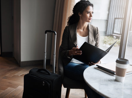 Sometimes youve got to travel to your goals. a young businesswoman reading through a business folder while waiting for her flight in an airport lounge.の写真素材