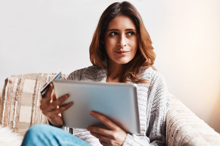 Can I afford this. an attractive young woman using a digital tablet and credit card on the sofa at...