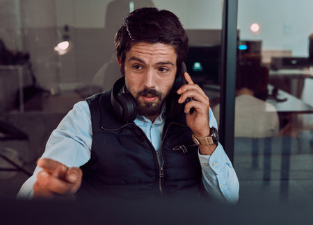Phone call, programmer and man talking in office, chatting and speaking to contact at night. Information technology, pointing and thinking male employee or coder with mobile smartphone for networkingの写真素材