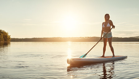 There is nothing more calm. an attractive young woman paddle boarding on a lake.の写真素材