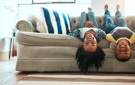 The sofa is a magical vehicle that transports us anywhere. a brother and sister hanging upside down off the sofa at home.の写真素材