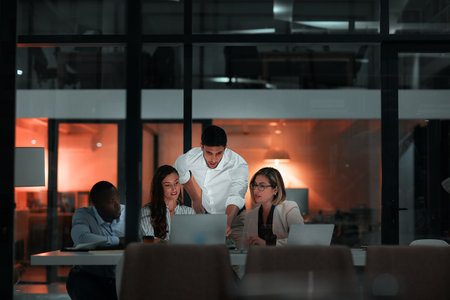 Team commitment around the clock. colleagues using a laptop together during a late night in a modern office.の写真素材