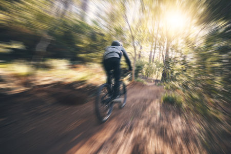 Energy, cycling, and speed with man in nature for training, extreme sports and motion blur. Workout, race and fast with cyclist on bike in forest park for performance, challenge and adventureの写真素材