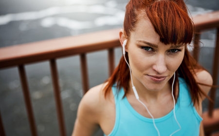Select your playlist and get your heart pumping to it. Portrait of a sporty young woman listening to music while out for a run in the city.の写真素材