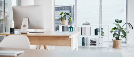 Empty office, interior and computer on desk in workplace, company or workspace. Room, desktop and table with corporate furniture, plants and window with modern design for business with nobody.の写真素材