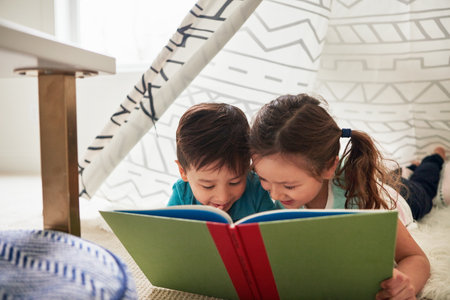 Theyre hooked to the story. two adorable young siblings reading a book together at home.の写真素材