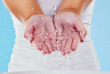 Water, washing and splash with hands of woman in studio for beauty, sustainability and skincare. Shower, cleaning and cosmetics with female in blue background for self care, spa and disinfectionの写真素材
