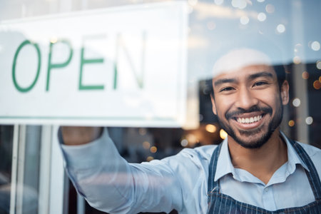Asian man, small business and portrait smile with open sign on window for service in coffee shop or restaurant. Male entrepreneur or manager with billboard or poster for opening retail store or cafeの写真素材