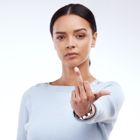 Woman, studio and middle finger portrait for angry, frustrated and rude emoji. Face of a serious female model with hand gesture for opinion, offended or anger and hate sign on a white backgroundの写真素材