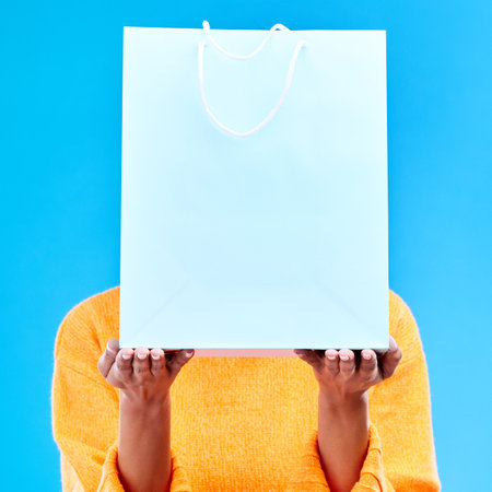 Shopping, bag and hands of woman on blue background for retail discount, deal and store promotion. Commerce mockup, fashion and girl holding package for advertising, sale news and purchase in studioの写真素材
