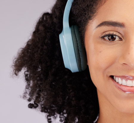 Headphones, happy woman and portrait of half face, studio background and backdrop. Closeup female model, smile and listening to music, sound and streaming media for audio connection, podcast or radioの写真素材