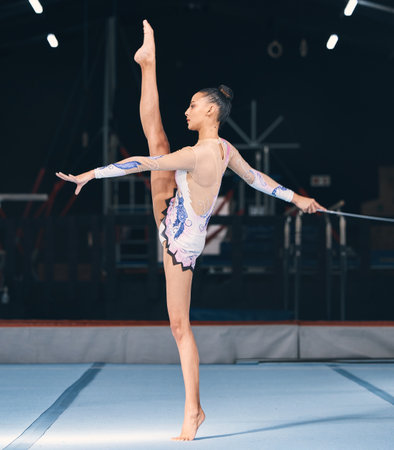 Ribbon, gymnastics and flexible woman in dance performance, balance legs and sports competition. Female, rhythmic movement and flexible dancing athlete, action and talent of creative concert in arenaの写真素材