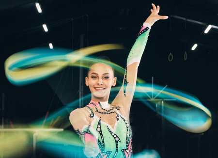 Ribbon gymnastics, happy woman and portrait of motion, dancing performance and competition in dark arena. Female dancer, rhythmic movement and solo routine of creative talent, sports concert or smileの写真素材