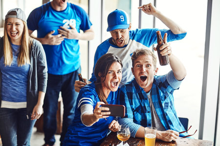 To the gridiron. A group of excited friends cheering on their favourite team at the bar.の写真素材