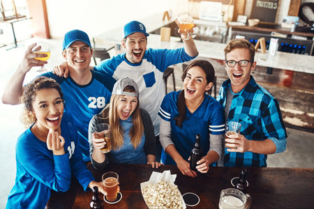 We support our sports. a group of friends having beers while watching a sports game at a bar.の写真素材