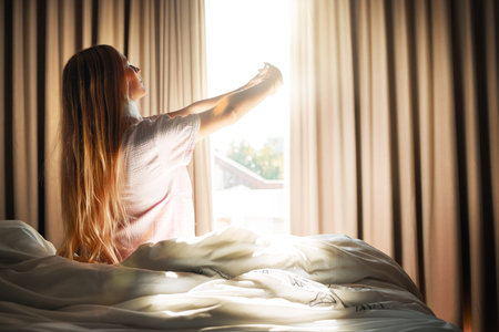 Stretch, calm and woman waking up in the morning to open the curtains in her bedroom at her apartment. Relax, peace and female stretching her arms while in bed getting ready to start her day at home.の写真素材