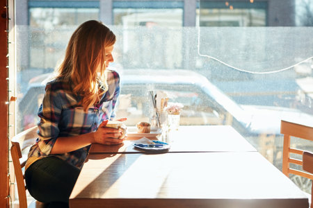 Enjoying some quiet time at her local cafe. an attractive young woman enjoying a cup of coffee in a cafe.の写真素材