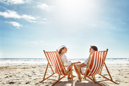 This feels like paradise. a mature couple relaxing together on deck chairs at the beach.の写真素材
