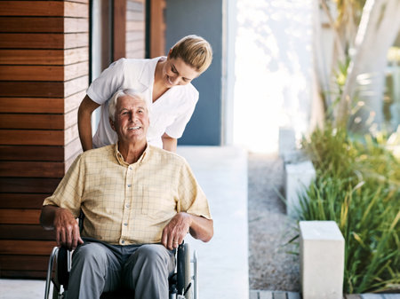 Out on a trip around the gardens. a nurse caring for a senior patient in a wheelchair outside a retirement home.の写真素材