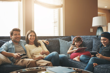 Weekends filled with no worries. a couple watching tv while their kids are busy using digital...