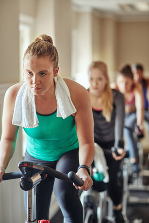 Get to sweating. a young woman working out with an exercise bike in a spinning class at the gym.の写真素材