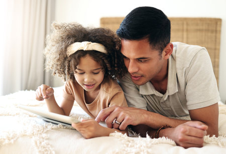 Tablet, learning child and father teaching for online development, home education and relax on bed. Dad or black man with girl on digital technology for internet game, helping and bonding togetherの写真素材