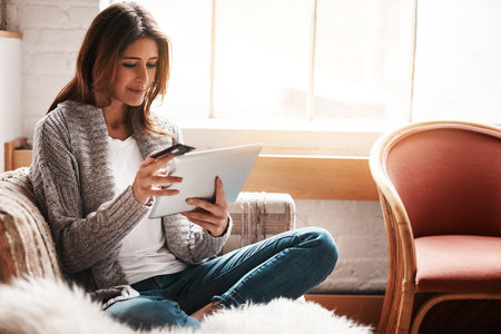 Less rush, more relaxing retail therapy. an attractive young woman using a digital tablet and credit card on the sofa at home.の写真素材
