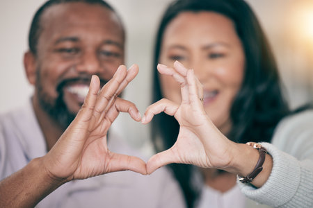Hands, love and heart with a couple in their home to relax together in the living room closeup. Hand gesture, emoji or romance with a senior man and woman bonding while sitting in their houseの写真素材