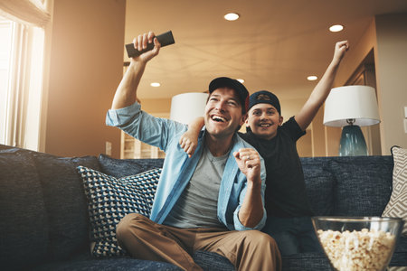 Father son bonding goals achieved. an enthusiastic father and son watching a sports match on tv at home.の写真素材
