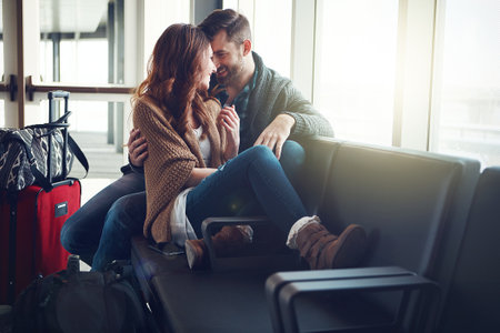 a young couple sitting in an airport with their luggage and embracing each other.の写真素材