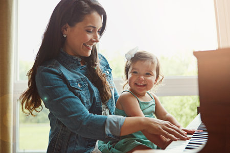 a mother playing the piano with her adorable little daughter at home.の写真素材