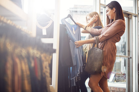 a young woman holding up an item that she picked out in a clothing store.の素材 [FY310202238215]