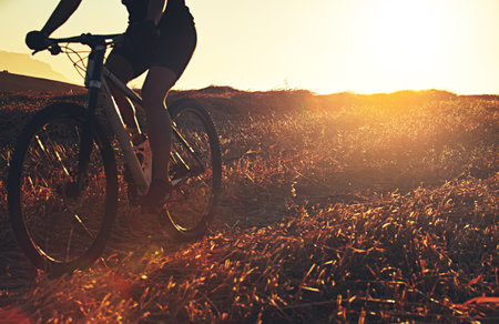 Cycling solo at sunset. an unidentifiable mountain biker out on a trail on a sunny day.の写真素材